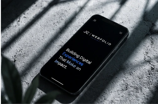 The JC Webfolio mobile site on a phone — the headline reads “Building digital experiences that make an impact.”